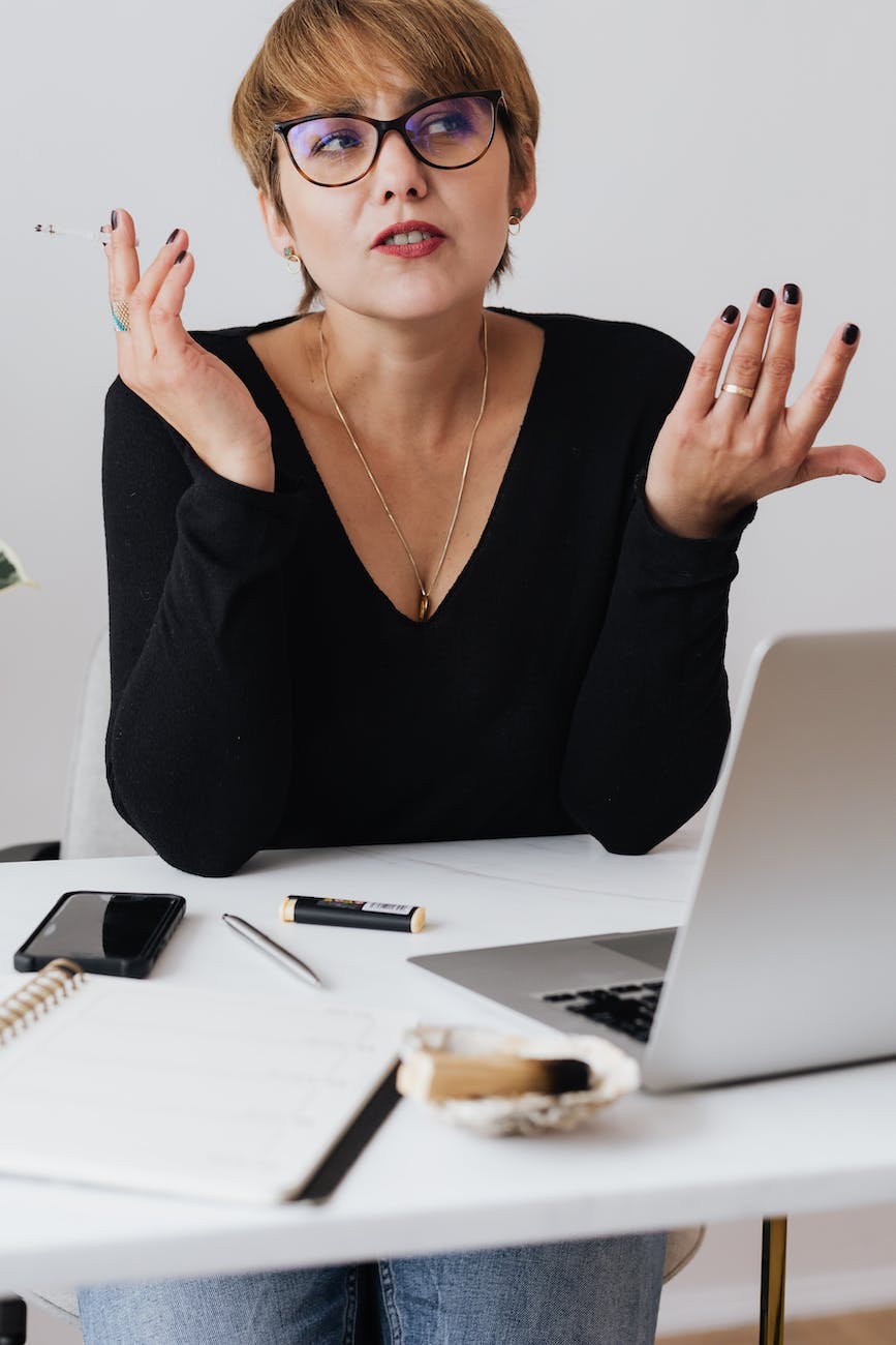 crop contemplative businesswoman sitting at desk and smoking cigarette